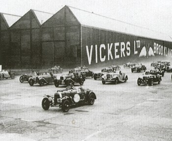 Carrera de automóviles en Brooklands con la factoría de Vickers de fondo (CC)
